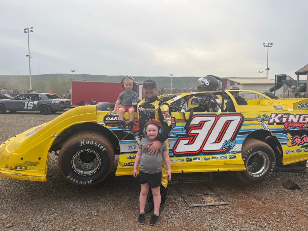 Ryan King at the track with Kamden sitting on the #30 and Kinsley standing in front of the car
